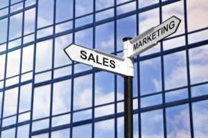 Concept image of Sales & Marketing on a signpost against a modern glass office building.