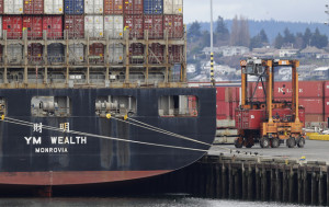 A cargo container mover carries a container at right next to a cargo ship operated by Yang Ming Marine Transport Corp. at the Port of Tacoma, Friday, Feb. 20, 2015, in Tacoma, Wash. With a Friday deadline looming, negotiators for the two sides in the contract dispute that has snarled international trade at U.S. West Coast seaports are laboring to reach a settlement as billions of dollars of cargo are sitting massive ocean-going ships anchored outside port facilities. (AP Photo/Ted S. Warren)