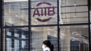 A woman wearing a face mask walks past a logo displayed at the Asian Infrastructure Investment Bank (AIIB) headquarters building in Beijing, China, on Thursday, Jan. 5 2017. One year after opening with 57 charter members, the China-led AIIB remains open to the U.S. joining, President Jin Liqun said. Photographer: Qilai Shen/Bloomberg