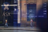 Pedestrians are reflected in a window in front of a board displaying stock prices at the Australian Securities Exchange (ASX) in Sydney, Australia, February 9, 2018.   REUTERS/David Gray