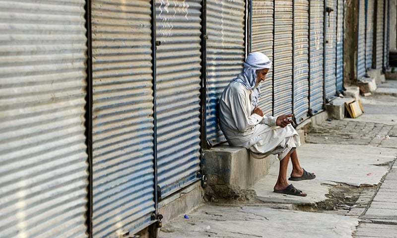 TOPSHOT - A Pakistani elderly man sits at a shuttered market during a traders countrywide strike against the prices hike, in Peshawar on July 13, 2019. (Photo by ABDUL MAJEED / AFP)