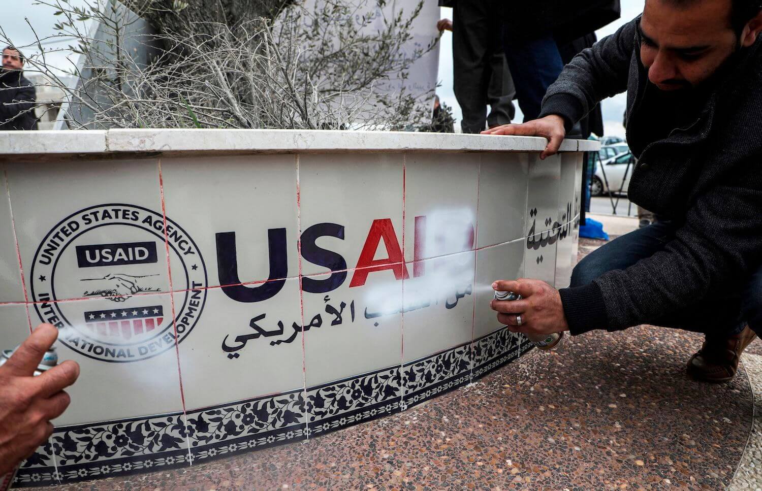 Palestinian protesters spray paint to cover the logo of the United States Agency for International Development (USAID), while protesting against US President Donald Trump's Middle East peace plan, in the city of Ramallah in the occupied West Bank on February 4, 2020. (Photo by ABBAS MOMANI / AFP) (Photo by ABBAS MOMANI/AFP via Getty Images)