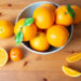 Top view of big bowl with bright oranges standing on wooden desk. Mandarin and cut tropical fruit laying on table. Studio shot. Nutrition and vegetarian concept